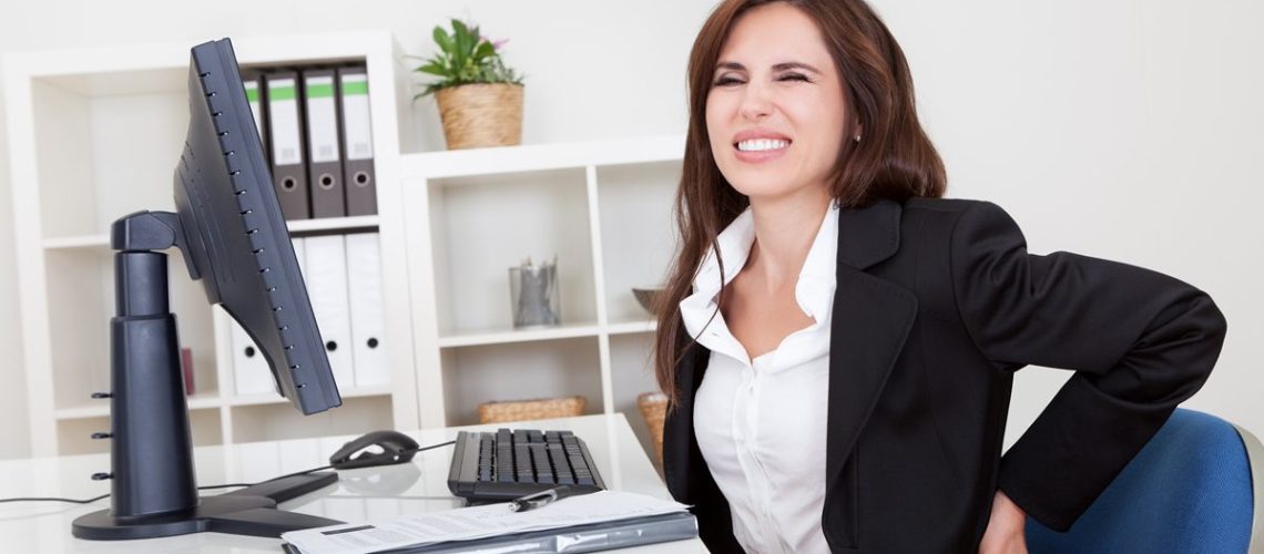 Young businesswoman having back pain while sitting at office desk