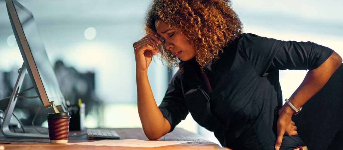 Shot of a young businesswoman suffering from backache while working at night